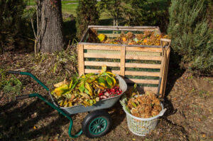 Home composting setup with single bin, wheelbarrow full of organic materials, and basket full of yard debris.