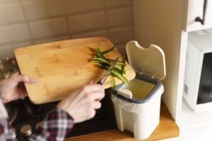 Arms of a person scraping green bean skins from a cutting board into a countertop compost bin.