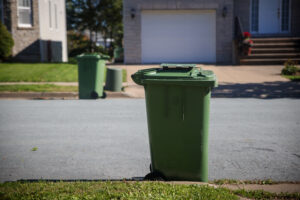 Green wheeled recycling cart at the curb on a sunny street with houses