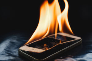 Burning smartphone with flames coming out of where the screen has burned and melted.