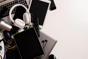 Offset to the left, pile of old electronics including laptops, tablets, and headphones that extends beyond the edge of the photo on the left but not the right.